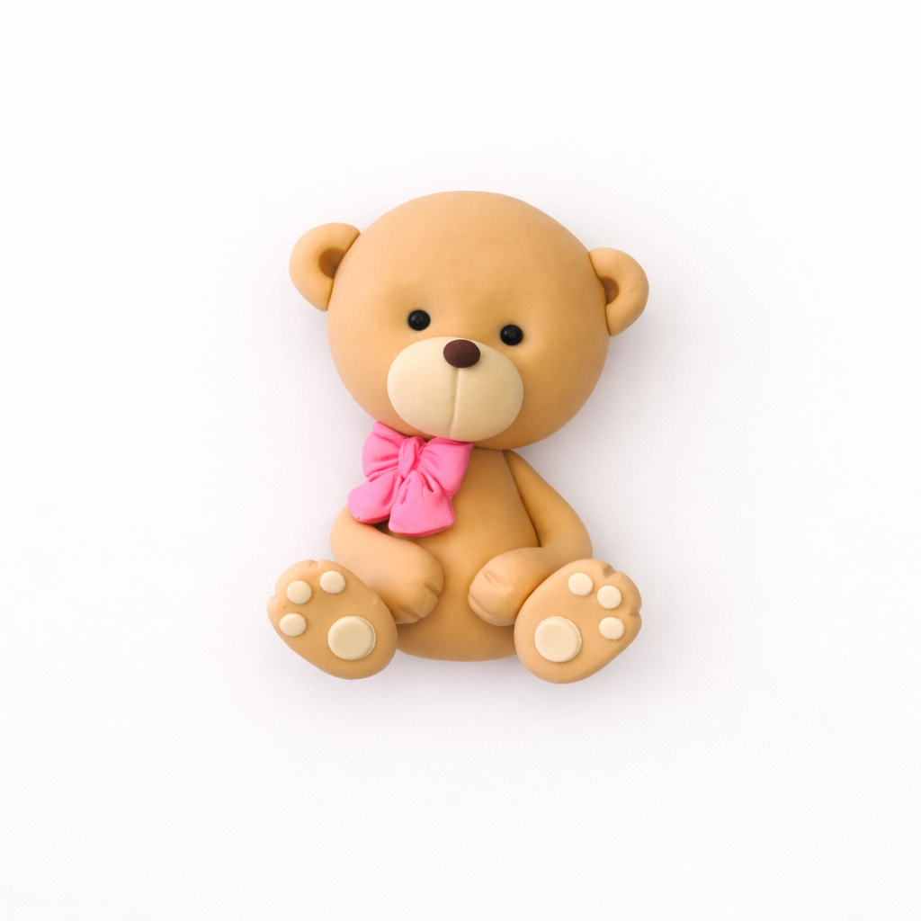 Fondant teddy bear cake topper with a pink bow tie on a white background