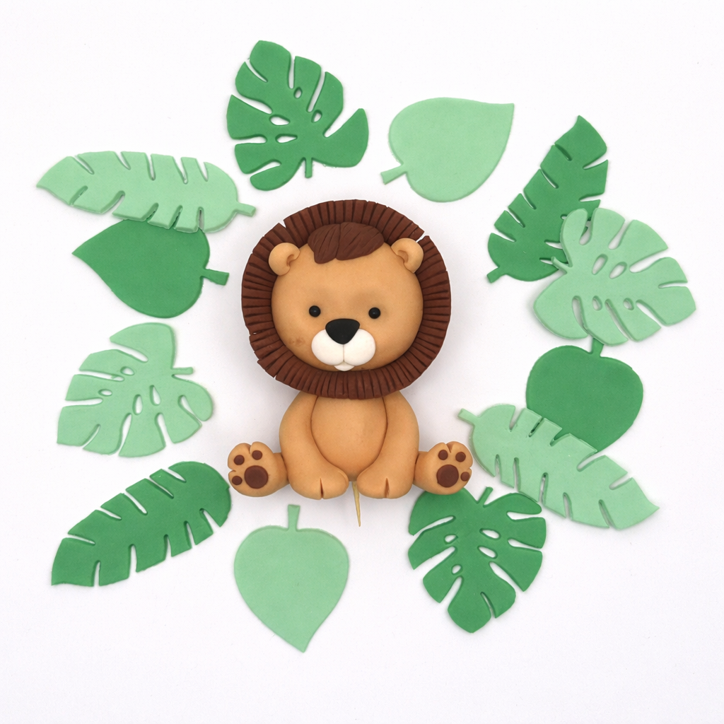 Fondant lion cake topper surrounded by fondant green leaves on a white background